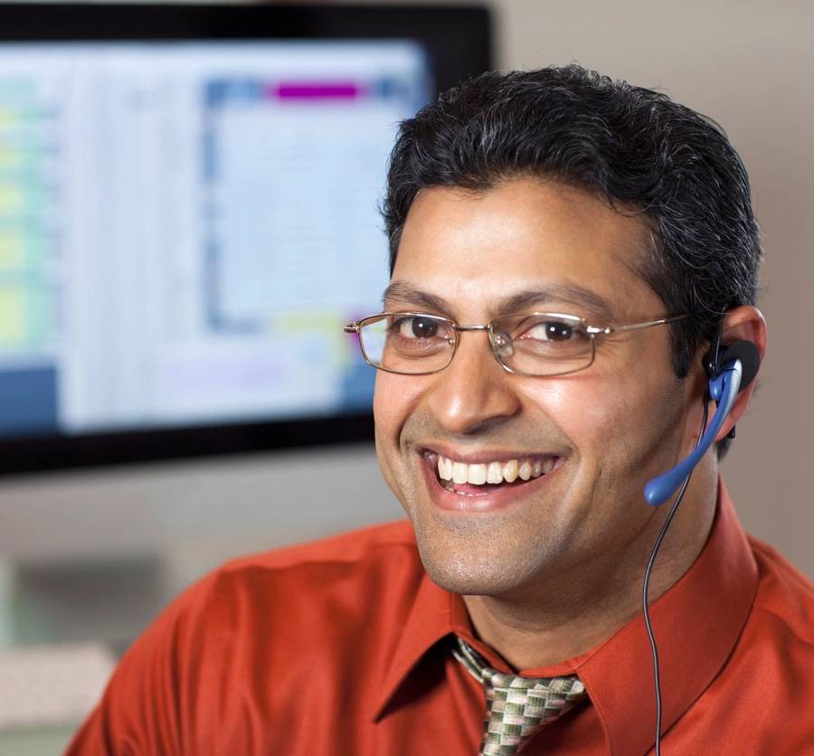 Smiling East Indian customer service rep with headset and computer monitor