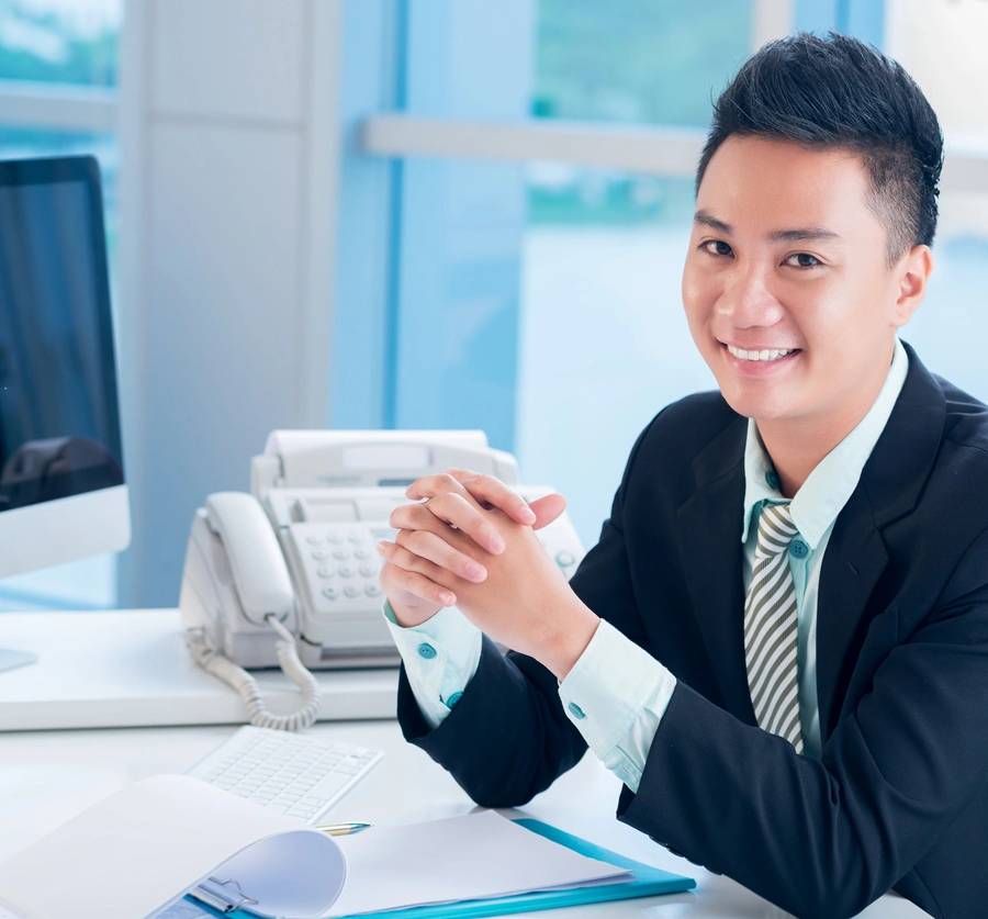 Close-up portrait of a financial broker at his workplace smiling and looking at camera on the foreground